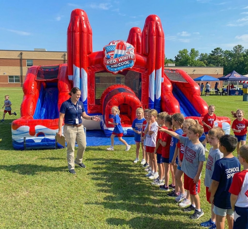 A friendly attendant supervising a line of excited children waiting to play on a large red, white, and blue bounce house rental at a Denver, CO school event.